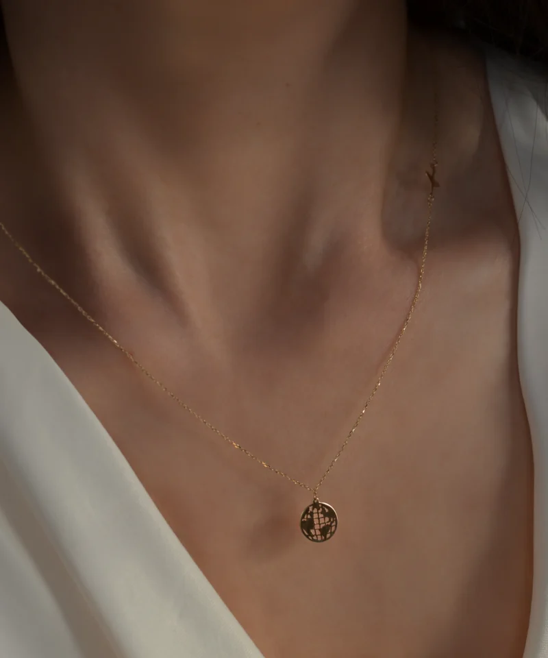 Delikatny złoty naszyjnik ankier z kulą ziemską i samolotem 585 na kobiecej szyi